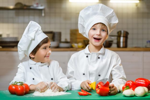 Funny happy chef boys cooking at restaurant kitchen.